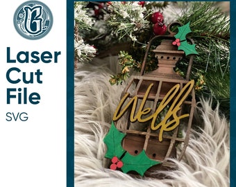 May include: A wooden Christmas ornament shaped like a lantern with the word "welcoming" written in gold lettering. The lantern has a holly sprig with red berries attached to it.