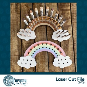 May include: Laser cut file for a rainbow-shaped marker holder with clouds. The rainbow has 18 holes for markers and the clouds have 10 holes each. The rainbow is painted in pastel colours and the clouds are white.