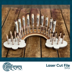 May include: A wooden rainbow-shaped stand with two cloud-shaped bases holds a collection of Crayola crayons in various shades of brown. The stand is designed to organise and display the crayons.