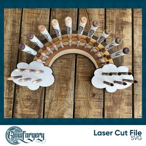 May include: A wooden rainbow-shaped organiser with two cloud-shaped compartments, designed to hold and display markers or crayons. The organiser is made of natural wood and has a rustic, farmhouse style.