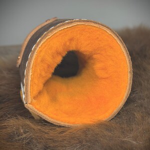 May include: A rolled-up cylindrical item, possibly a case or holder, with a dark brown leather exterior and a bright orange, fluffy interior. White stitching and a lighter brown trim are visible. The item is well-crafted.