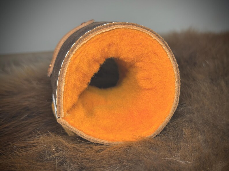 May include: A rolled-up cylindrical item, possibly a case or holder, with a dark brown leather exterior and a bright orange, fluffy interior. White stitching and a lighter brown trim are visible. The item is well-crafted.