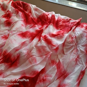 May include: White fabric with red tie-dye pattern. The fabric is crumpled and has a soft, flowing texture. "Shot on OnePlus" and "By vinayak textile" are printed at the bottom of the image.