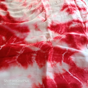 May include: White fabric with red tie-dye pattern. The fabric is wrinkled and has a soft, flowing texture. "Shot on OnePlus" and "By vinayak textile" are printed at the bottom of the image.