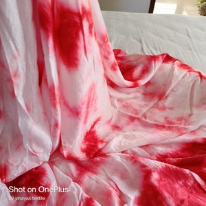 May include: White fabric with red tie-dye pattern. The fabric is folded and draped on a white surface. "Shot on OnePlus" and "By vinayak textile" are printed at the bottom of the image.