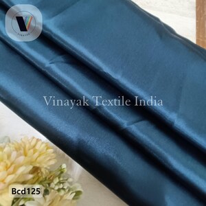 May include: A close-up of a teal blue satin fabric. The fabric is smooth and shiny. The text "Bcd125" is visible in the bottom left corner of the image.