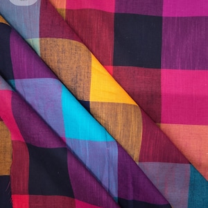 May include: A fabric featuring a large-scale plaid pattern in vibrant shades of magenta, deep purple, bright yellow, turquoise, and black. The textile displays a visible woven texture with folds creating depth. The text Ctnf074 is printed at the bottom.