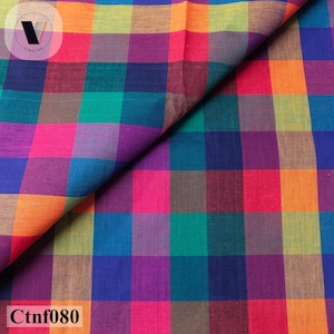 May include: A fabric featuring a vibrant multi-colored plaid pattern with squares in shades of orange, yellow, magenta, purple, teal, and blue. The textile displays a consistent grid design throughout, with a folded corner revealing the texture.