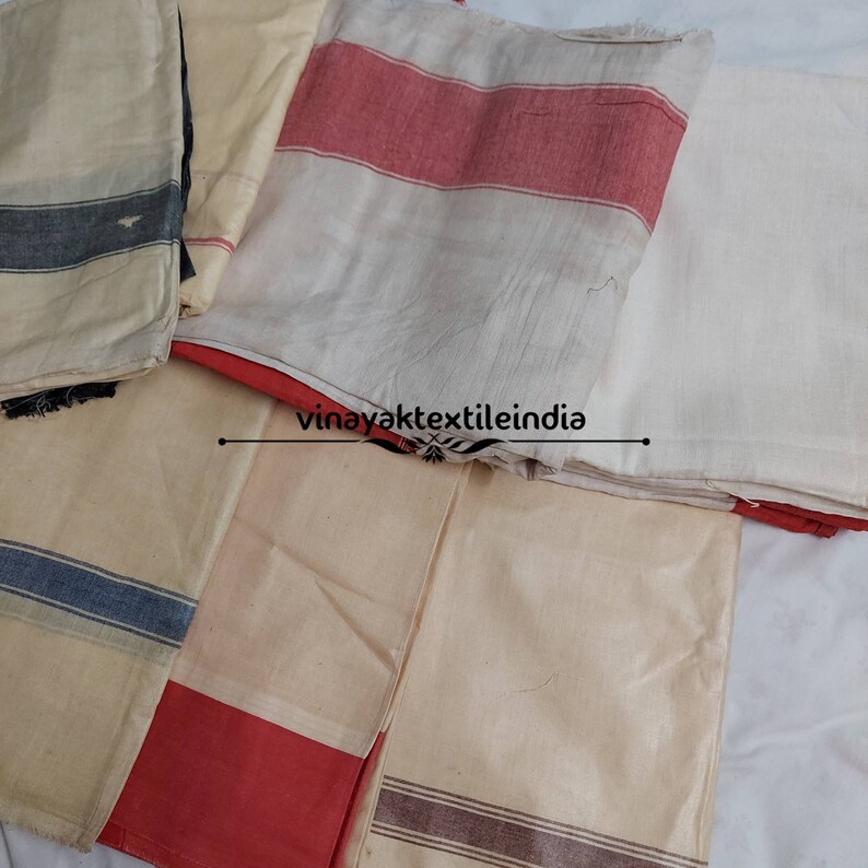 Pode incluir: V&aacute;rias pe&ccedil;as de tecido dobradas, em branco sujo, com riscas e bordas vermelhas, azuis e castanhas. O texto "vinayaktextileindia" &eacute; vis&iacute;vel na imagem.