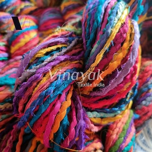 May include: A close-up of a colourful yarn made from recycled fabric scraps. The yarn is a mix of bright colours, including pink, purple, blue, green, and yellow. The yarn is twisted together to create a thick, textured rope. The yarn is labelled "Vinayak Textile India".