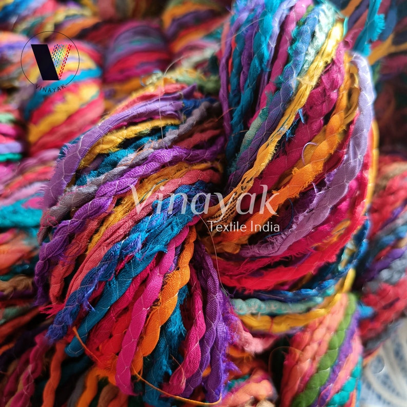 May include: A close-up of a colourful yarn made from recycled fabric scraps. The yarn is a mix of bright colours, including pink, purple, blue, green, and yellow. The yarn is twisted together to create a thick, textured rope. The yarn is labelled "Vinayak Textile India".
