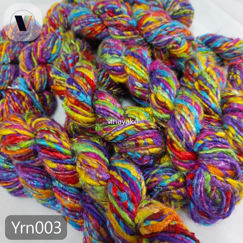 May include: Close-up of colorful yarn in shades of purple, yellow, blue, and red. The yarn is thick and textured, with a braided appearance. The text "Yrn003" is in the bottom left corner. The yarn is likely used for knitting or other fiber crafts.