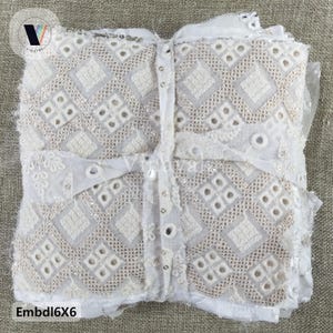 May include: White fabric with a geometric pattern of small squares and circles. The fabric is layered and has a slightly distressed look. The text "Embd16X6" is visible in the bottom left corner.