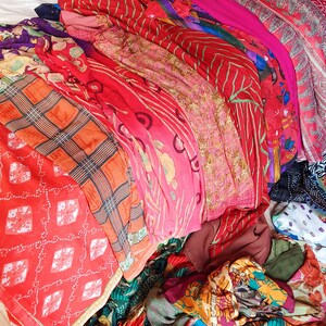 May include: A collection of folded fabric pieces featuring a variety of patterns and colours, including bright red, orange, pink, and purple. The textiles display diverse designs such as floral motifs, geometric plaid, and intricate paisley prints.