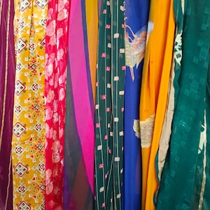 May include: A collection of hanging fabric panels featuring a variety of colours and patterns, including a yellow panel with geometric shapes, a red floral print, a pink and purple striped section, a dark green grid pattern, and a solid yellow drape.