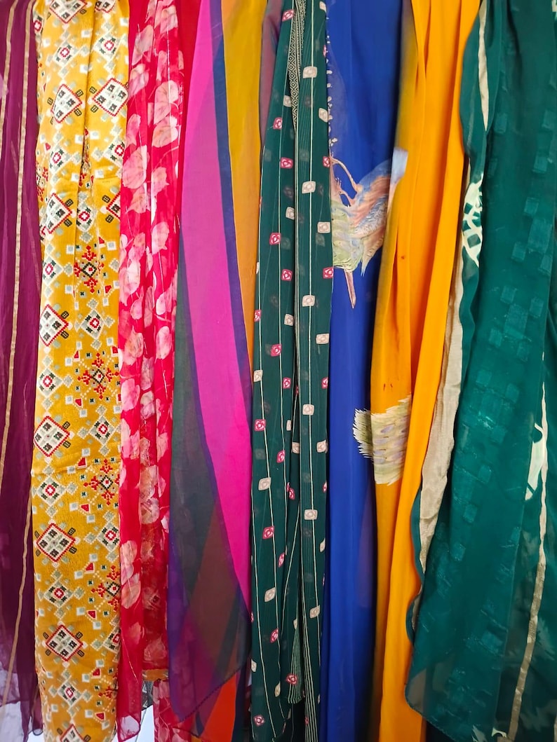 May include: A collection of hanging fabric panels featuring a variety of colours and patterns, including a yellow panel with geometric shapes, a red floral print, a pink and purple striped section, a dark green grid pattern, and a solid yellow drape.