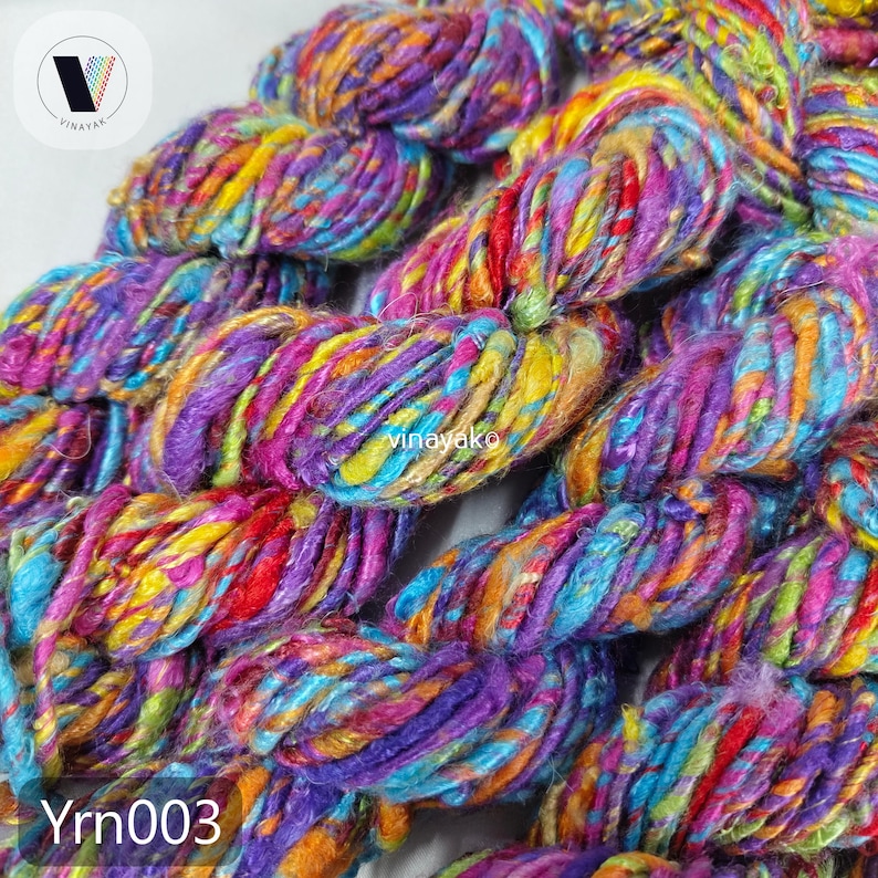 May include: Close-up of colorful yarn in shades of purple, blue, yellow, and red. The yarn is thick and textured, with a mix of colors throughout. The text "Yrn003" is visible in the bottom left corner.