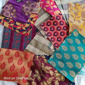 Puede incluir: Una colección de muestras de tela en varios colores y patrones, incluyendo dorado, rojo, morado, turquesa y marrón. Las telas presentan diseños intrincados con motivos paisley, florales y geométricos. El texto "Shot on OnePlus" y "By Vinayak textile" es visible en la parte inferior de la imagen.