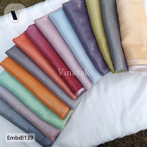 May include: A collection of 12 fabric swatches in various colors, including gold, silver, red, orange, green, blue, and purple. The fabric has a subtle shimmer and a textured, woven pattern. The swatches are arranged in a fan shape, with the text "Vinayak" visible in the center.