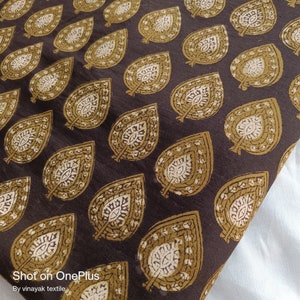 May include: Brown fabric with a repeating pattern of gold leaf designs. The fabric has a subtle texture and a slightly distressed look.