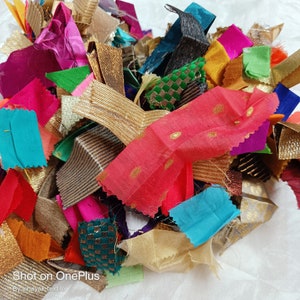 Può includere: Un mucchio di ritagli di stoffa colorati in varie trame e motivi, tra cui oro, rosa, blu, verde e marrone. I ritagli sono disposti in ordine casuale, creando una composizione visivamente accattivante e testurizzata.