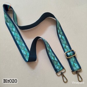 May include: A dark teal shoulder strap with a geometric pattern of teal and green triangles. The strap has metal swivel hooks and a rectangular buckle. The text "Blt020" is visible.