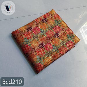 Puede incluir: Una pieza de tela cuadrada con un patr&oacute;n geom&eacute;trico repetitivo de estrellas y motivos de hojas en tonos rojo, naranja, dorado, morado y verde azulado. El tejido tiene un brillo met&aacute;lico y lleva el texto Bcd210 en la esquina.
