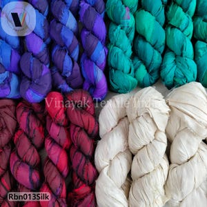 Könnte beinhalten: Nahaufnahme von farbenfrohen Seidenstoffbündeln in Lila, Blau, Grün, Rot und Creme. Der Stoff ist verdreht und scheint handgefärbt zu sein. Der Text "Rbn013Silk" ist sichtbar.