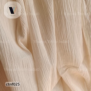 Może przedstawiać: Zbliżenie na jasnobeżowy materiał o pomarszczonej fakturze. Materiał jest udrapowany i złożony, co pokazuje jego miękkość i płynność. Tekst "ctnf025" jest widoczny w lewym dolnym rogu obrazu.