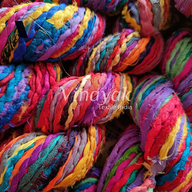 May include: Close-up of a colourful bundle of yarn made from recycled fabric scraps. The yarn is a mix of bright colours, including red, orange, yellow, green, blue, purple, and pink. The yarn is twisted together to create a thick, textured rope.