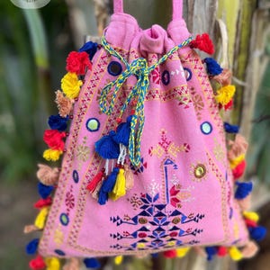 Puede incluir: Bolso rosa con cordón y coloridos patrones geométricos bordados, pequeños espejos y borlas. El bolso tiene un cierre de cordón y una correa rosa. El texto "Bag037" es visible en la parte inferior.
