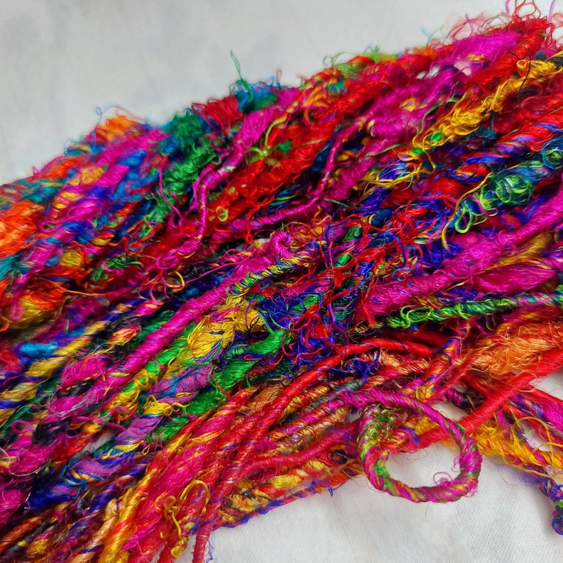 K&ouml;nnte beinhalten: Ein Haufen bunter, mehrfarbiger und strukturierter Seidenf&auml;den. Das Garn ist eine Mischung aus leuchtendem Pink, Rot, Orange, Gelb, Gr&uuml;n, Blau und Lila.