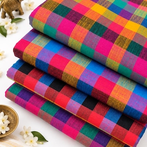 May include: A stack of four folded fabric pieces featuring a vibrant multi-colored plaid pattern. The textile displays a repeating grid of bright yellow, hot pink, deep teal, royal blue, and black squares, showcasing a woven texture throughout.
