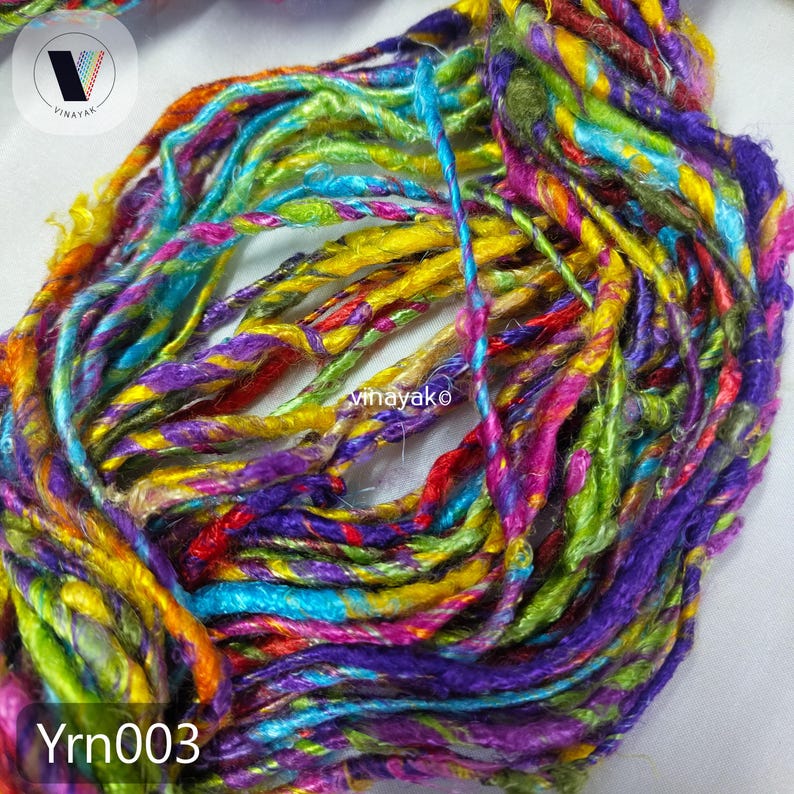 May include: Close-up of a vibrant bundle of yarn in a spectrum of colors including yellow, green, purple, and red. The yarn is twisted and textured, with the text "Yrn003" at the bottom. The logo "Vinayak" is in the top left.