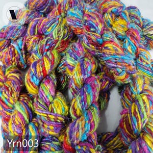 May include: Close-up of colorful yarn in shades of purple, yellow, blue, green, and red. The yarn is twisted and braided, with the text "Yrn003" visible in the bottom left corner. The yarn is from vinayako.