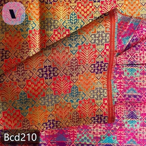 Puede incluir: Un textil vibrante con un patr&oacute;n geom&eacute;trico detallado en tonos de rojo, naranja, dorado, azul y morado. La tela presenta un dise&ntilde;o repetitivo de hojas estilizadas y formas de diamante. El texto "Bcd210" es visible en la parte inferior.