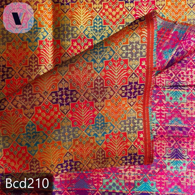 Puede incluir: Un textil vibrante con un patr&oacute;n geom&eacute;trico detallado en tonos de rojo, naranja, dorado, azul y morado. La tela presenta un dise&ntilde;o repetitivo de hojas estilizadas y formas de diamante. El texto "Bcd210" es visible en la parte inferior.