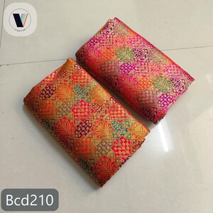 Puede incluir: Dos piezas de tela dobladas con intrincados patrones geom&eacute;tricos en tonos naranja, rojo, dorado, morado y verde. La tela tiene un aspecto brillante y texturizado. El texto "Bcd210" es visible en la parte inferior.