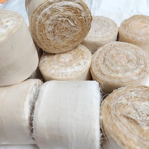 Könnte beinhalten: Nahaufnahme einer Gruppe von beige und cremefarbenen Stoffrollen. Die Rollen bestehen aus einem weichen, natürlichen Material und haben eine leicht strukturierte Oberfläche.