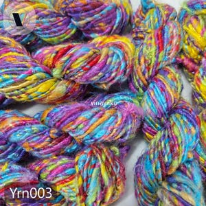 May include: Close-up of colorful yarn skeins. The yarn is a mix of vibrant colors including yellow, purple, blue, and red. The text "Yrn003" is visible at the bottom left. The yarn appears to be soft and textured, suitable for knitting or crochet projects.