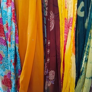 May include: A collection of five hanging fabric panels featuring diverse designs. The first is a blue floral print, the second is solid mustard yellow, the third is a dark maroon with botanical patterns, the fourth is yellow with pink tie-dye, and the fifth is a dark green with gold trim.