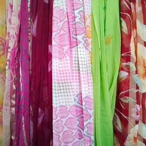 May include: A collection of vertical fabric scarves featuring diverse patterns and colours, including a pink tie-dye, a solid deep maroon, a white scarf with pink leaves and geometric shapes, a solid lime green, and a red floral print.