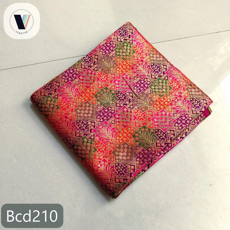 Puede incluir: Cuadrado de tela doblado con un patr&oacute;n vibrante e intrincado en tonos de rosa, morado, naranja y verde. El dise&ntilde;o presenta elementos geom&eacute;tricos y florales con acentos dorados. El texto "Bcd210" es visible.