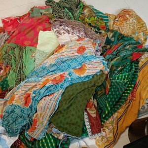 May include: A large, disorganised pile of assorted fabric pieces featuring a variety of patterns and colours. The collection includes textiles in shades of green, red, orange, yellow, and blue, with floral, geometric, and abstract prints throughout.