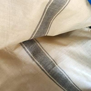 Pode incluir: Tecido creme com detalhe de riscas cinzentas. O tecido parece estar dobrado, mostrando a textura e o padr&atilde;o. As riscas s&atilde;o de largura m&eacute;dia e percorrem o comprimento do tecido.
