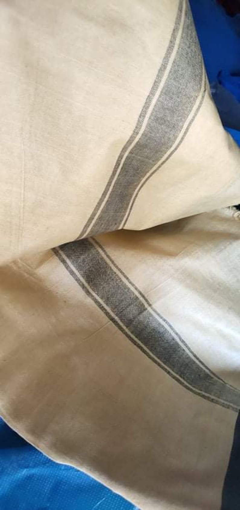 Pode incluir: Tecido creme com detalhe de riscas cinzentas. O tecido parece estar dobrado, mostrando a textura e o padr&atilde;o. As riscas s&atilde;o de largura m&eacute;dia e percorrem o comprimento do tecido.