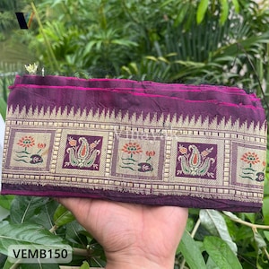 May include: A folded length of fabric in shades of purple and gold. The fabric features a repeating pattern of floral and paisley designs within rectangular frames. The text "VEMB150" is visible.