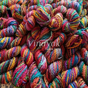 May include: A close-up of a pile of colourful, hand-spun yarn made from recycled fabric scraps. The yarn is twisted and knotted, creating a textured and vibrant look. The yarn is labelled "Vinayak Textile India".