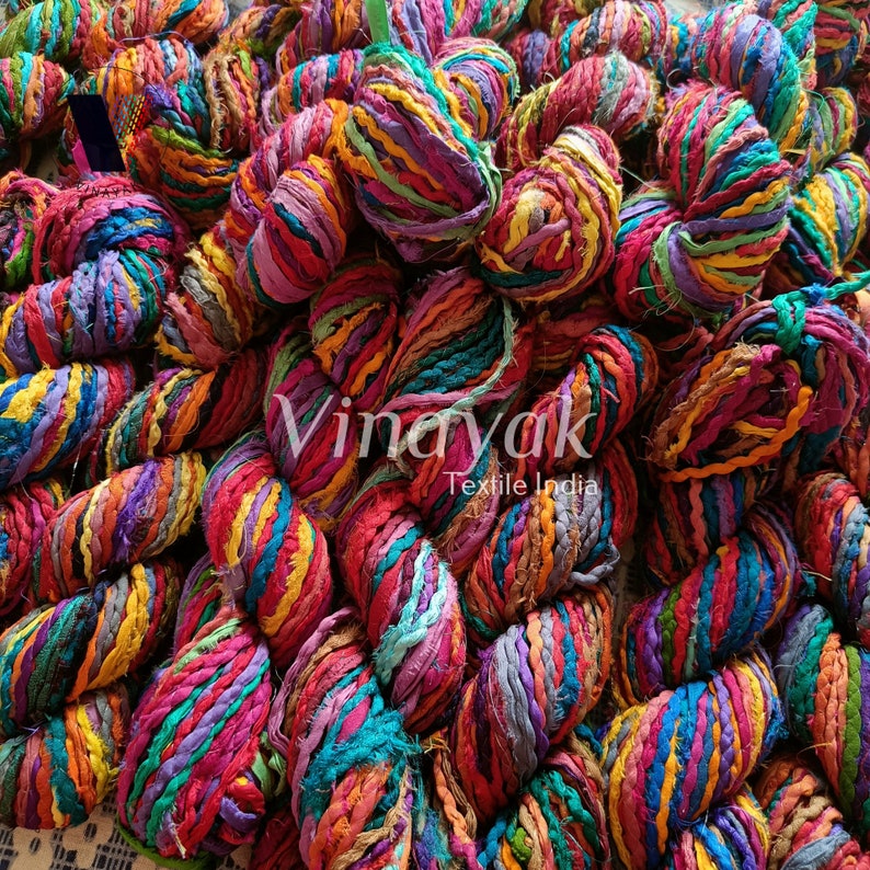 May include: A close-up of a pile of colourful, hand-spun yarn made from recycled fabric scraps. The yarn is twisted and knotted, creating a textured and vibrant look. The yarn is labelled "Vinayak Textile India".