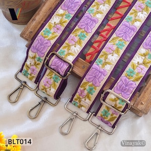 May include: Embroidered bag straps with a floral design. The straps feature a purple background with embroidered flowers in shades of purple, pink, green, and white. Each strap has metal clasps and buckles for attachment. The product code "BLT014" is visible.